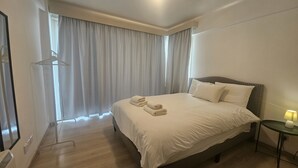 A hotel room with a large bed, a bedside table with a lamp, a window with curtains, and a coat rack.