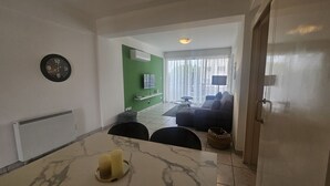 A modern living room with a green accent wall, a flat-screen TV, a sofa, and a dining area with a marble table.