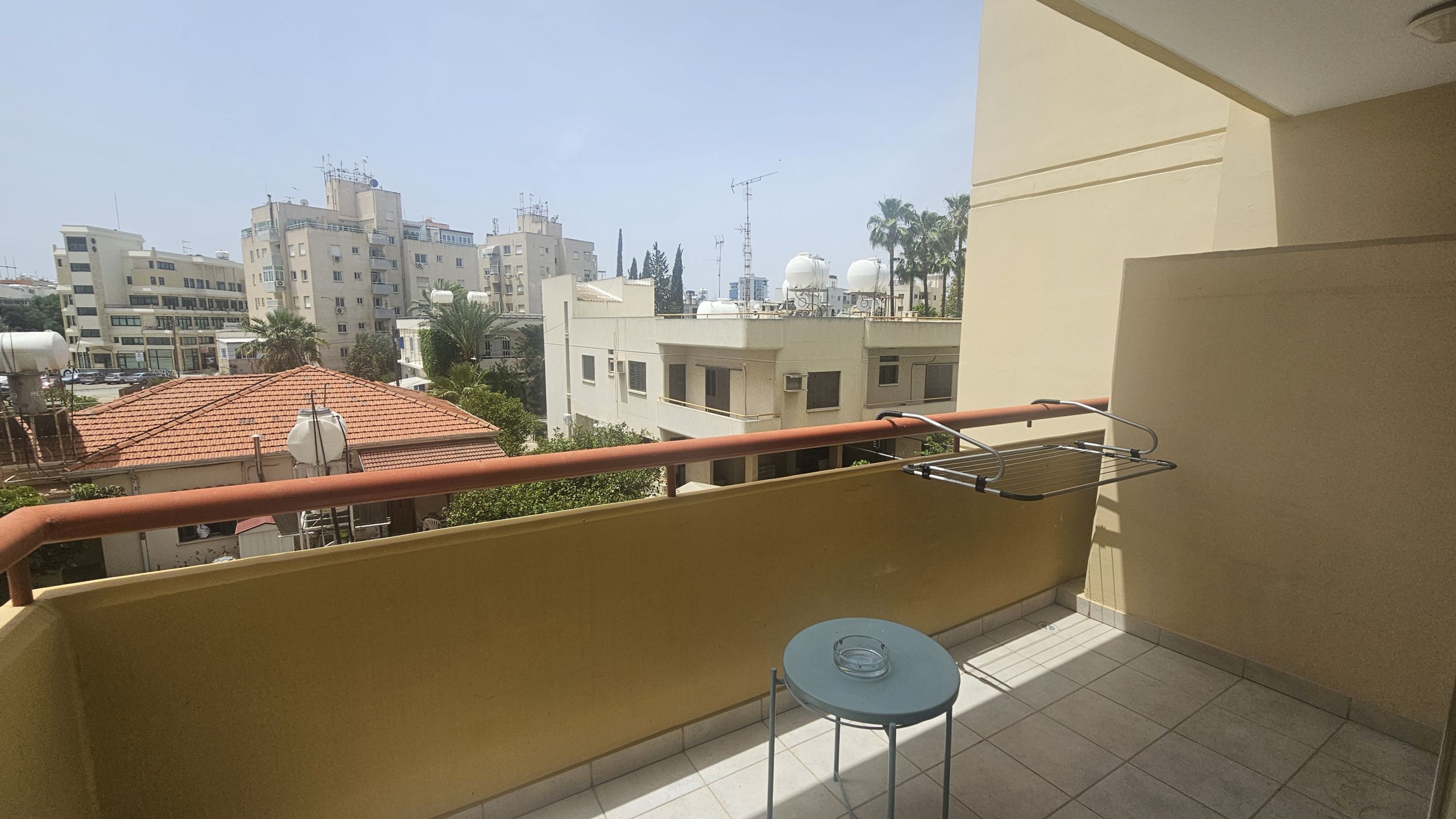 Un balcon avec une petite table et un étendoir métallique.