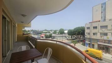 A balcony with a table and chairs, overlooking a street with buildings and a yellow delivery truck.