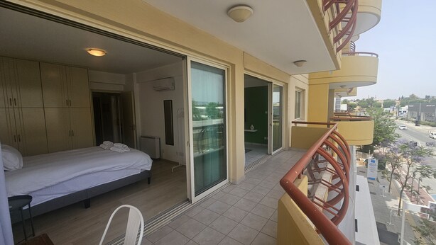A balcony with a bed, sliding glass doors, and a view of the street.