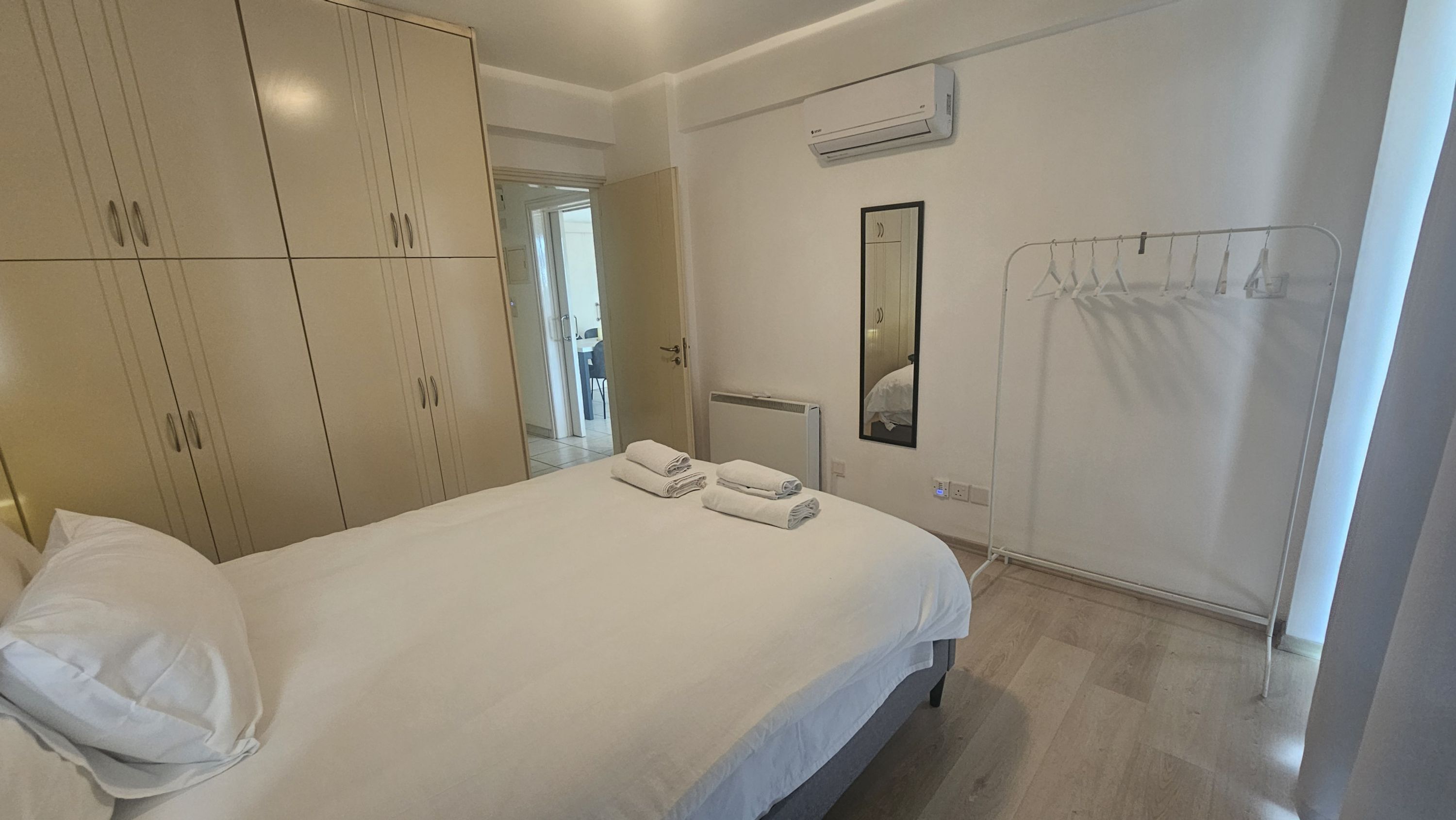 Habitación de hotel con cama, armario, unidad de aire acondicionado, espejo y perchero.