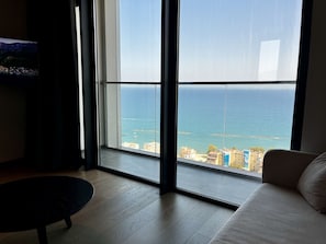 A room with a large window offering a view of the sea and buildings.
