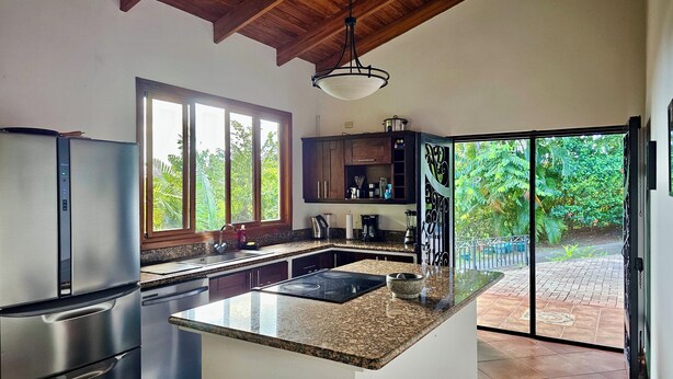 A kitchen with a granite countertop, stainless steel appliances, and a view of a garden through a sliding glass door. - Feel-good oasis Playa Sámara, Ocean view, Private pool, King bed, Dishwasher (Sámara)