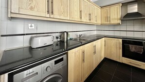 Eine Küche mit Holzausstattung, einer Daewoo Waschmaschine, einem Toaster und einem Wasserkocher.