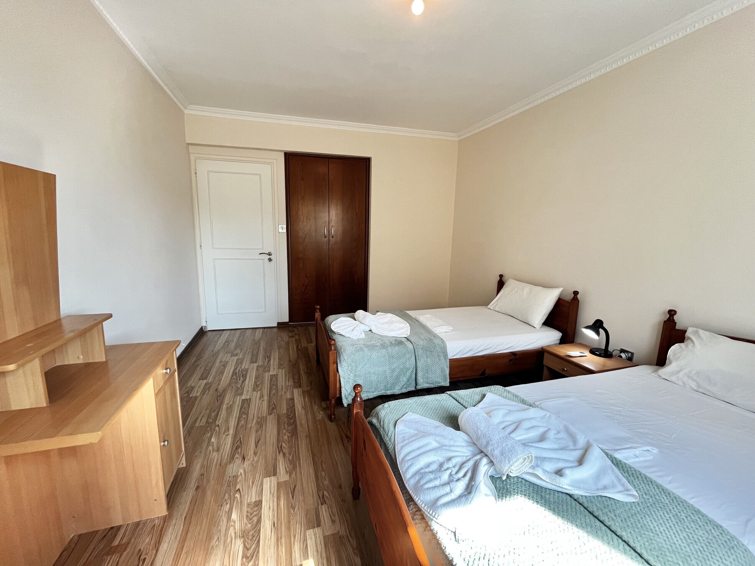 A hotel room with two beds, a wooden wardrobe, a desk, and a door.