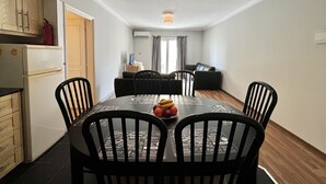 Ein kompakter Wohnbereich mit Essplatz, inklusive Tisch und Stühlen, Küchenzeile mit Schränken und Kühlschrank sowie einer Sitzecke mit Sofa und Vorhängen.