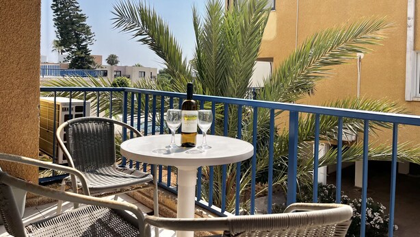 Ein Balkon mit rundem Tisch, zwei Stühlen, einer Weinflasche und Gläsern.