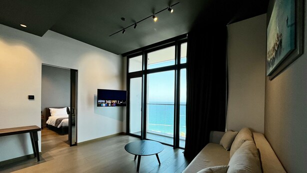 A modern living room with a large window, a flat-screen TV, a sofa, and a small table. - 128 LIM - 2106 Stay Only Tower Suite (Limassol)