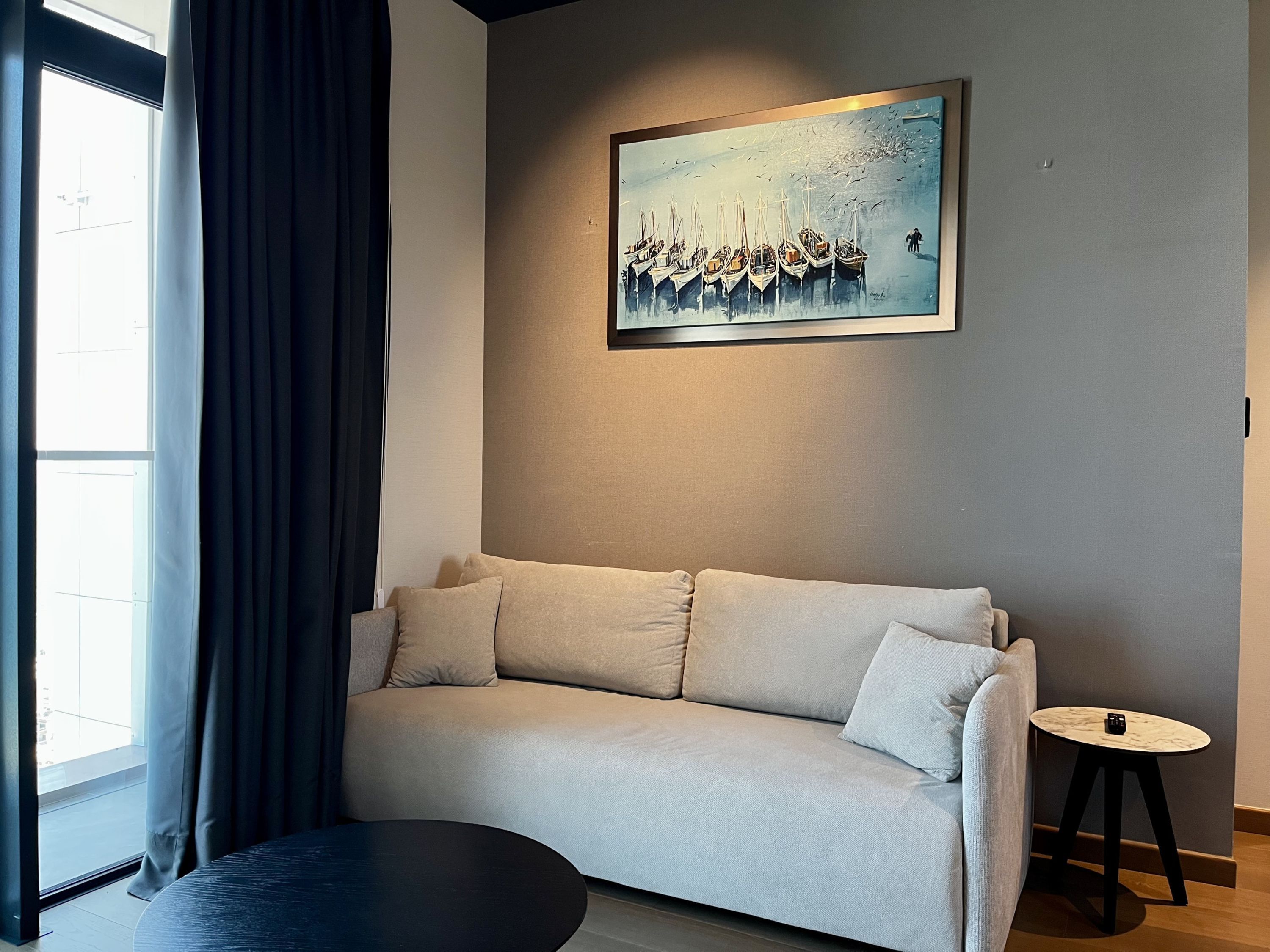 A modern living room with a sofa, a round coffee table, and a painting of boats on the wall.