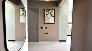 A modern hallway with a large mirror, two framed artworks, a door, and a ceiling light. - STAY Mouson View Apartment (Limassol)