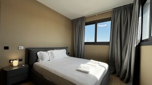 A hotel room with a large bed, a bedside table with a lamp, a thermostat, and a window with curtains. - STAY Mouson View Apartment (Limassol)
