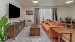 A modern living room with a sofa, coffee table, TV, and a dining area with chairs and a table. - Downtown 1 Bedroom Flat with Views (Anchorage)