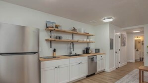 A modern kitchen with white cabinets, a stainless steel refrigerator, wooden shelves, and a wooden countertop. - Downtown 1 Bedroom Flat with Views (Anchorage)