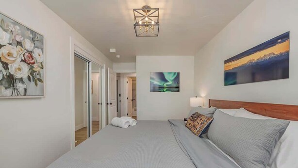 Habitación de hotel con una cama grande, cabecera de madera, mesita de noche y un cuadro de un paisaje montañoso.