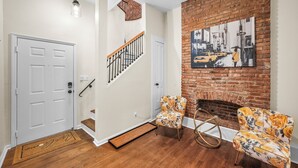 A living room with a brick fireplace, two floral armchairs, a white door, and a staircase.