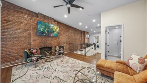 A living room with a brick wall, a fireplace, a ceiling fan, and a sofa.