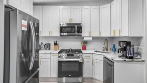 A modern kitchen with white cabinets, stainless steel appliances, and gold handles.