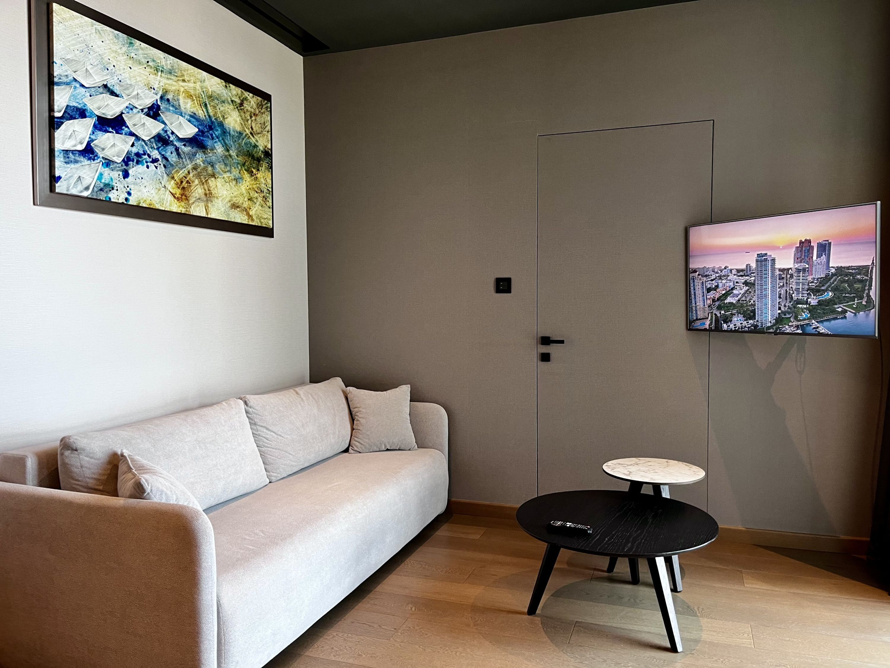 A modern living room with a sofa, a small round table, a TV mounted on the wall, and a door.