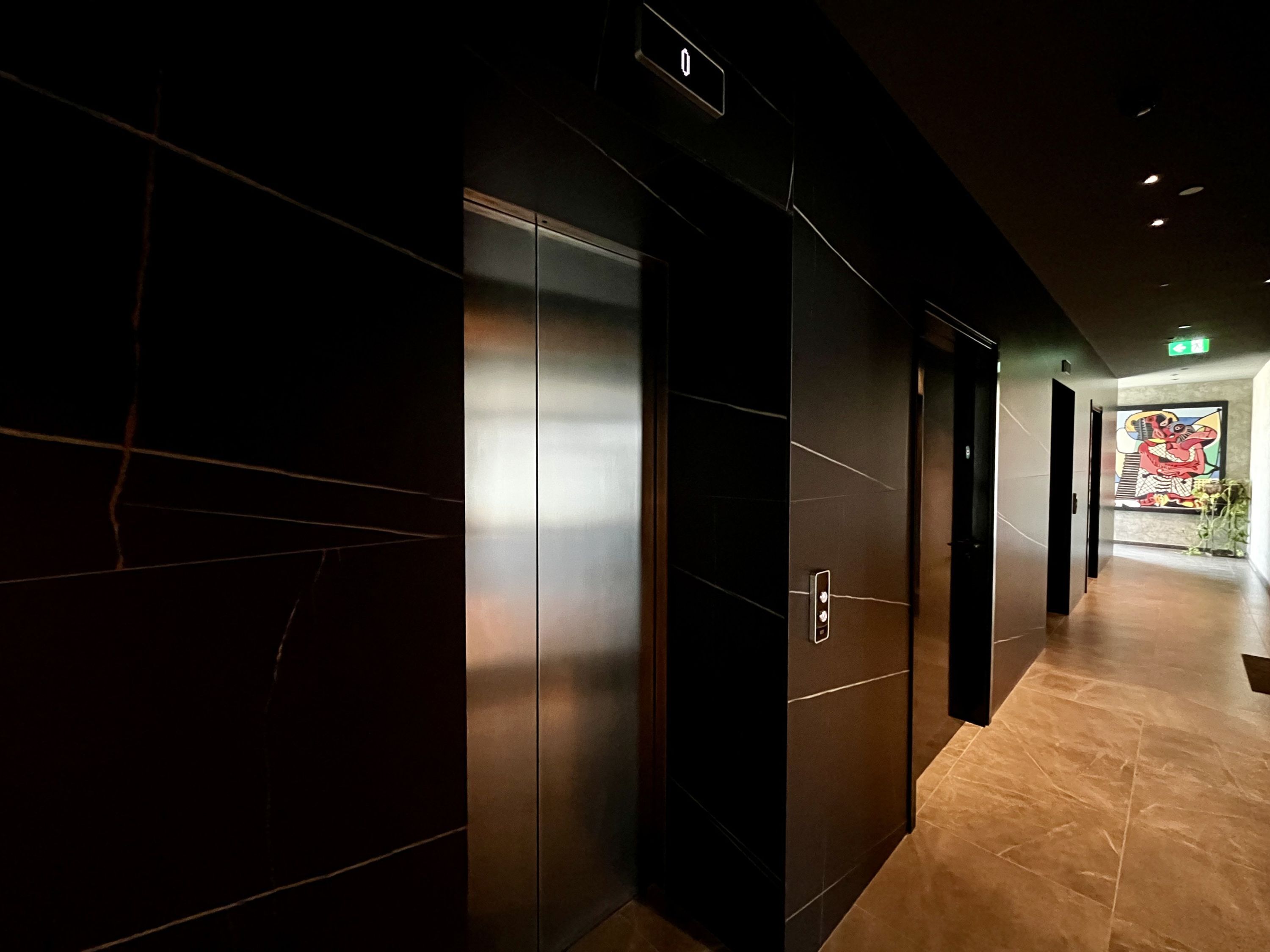 A modern hallway with a marble floor, a wall-mounted elevator, and a colorful mural in the background.