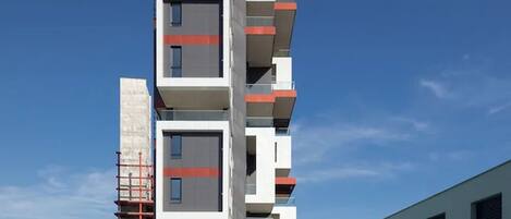 Un edificio moderno de varios pisos con balcones, piscina y cielo azul despejado.