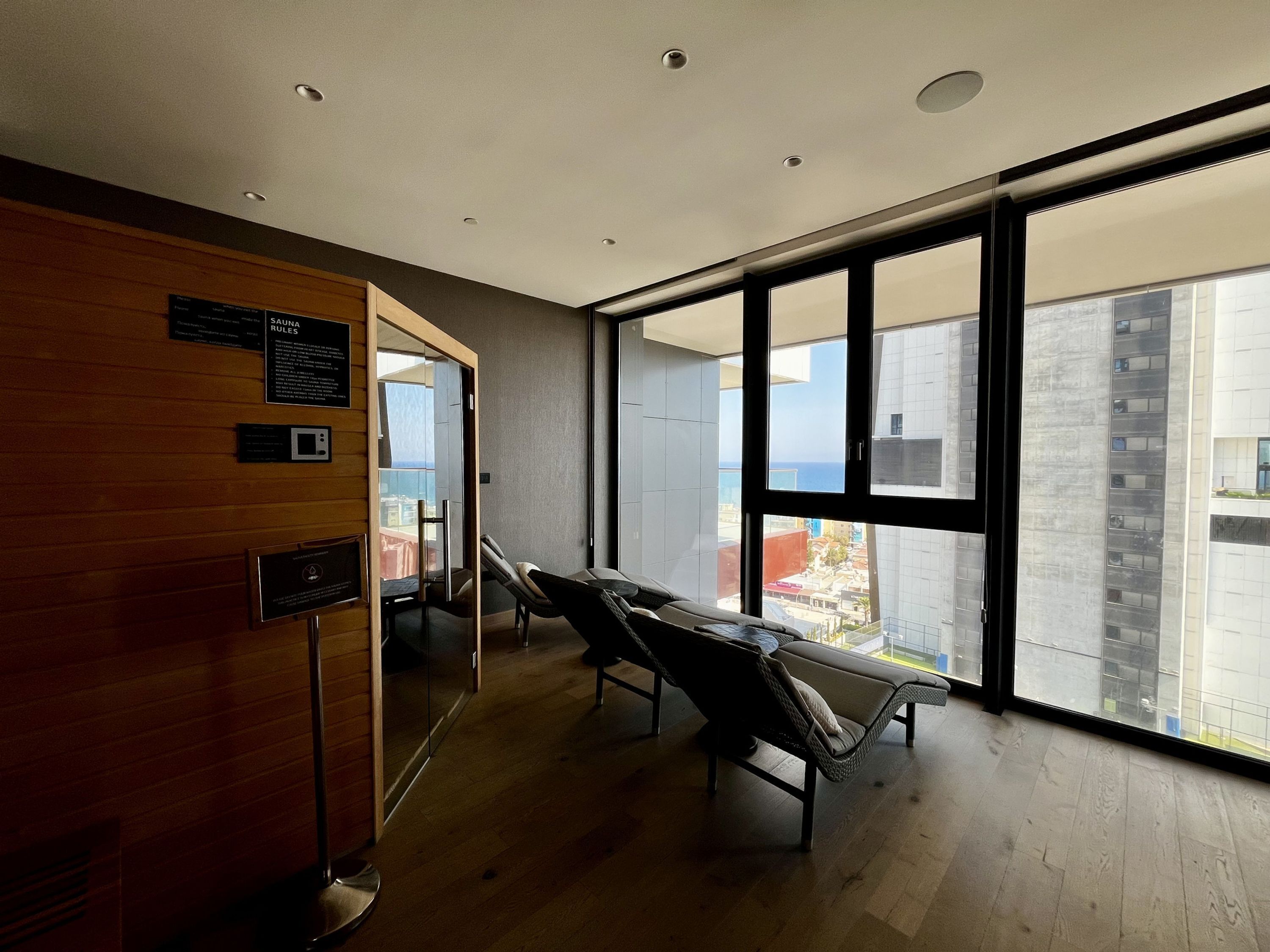 Ein Spa-Raum mit Holzwand, einer Massageliege und einem großen Fenster mit Blick auf Gebäude und das Meer.