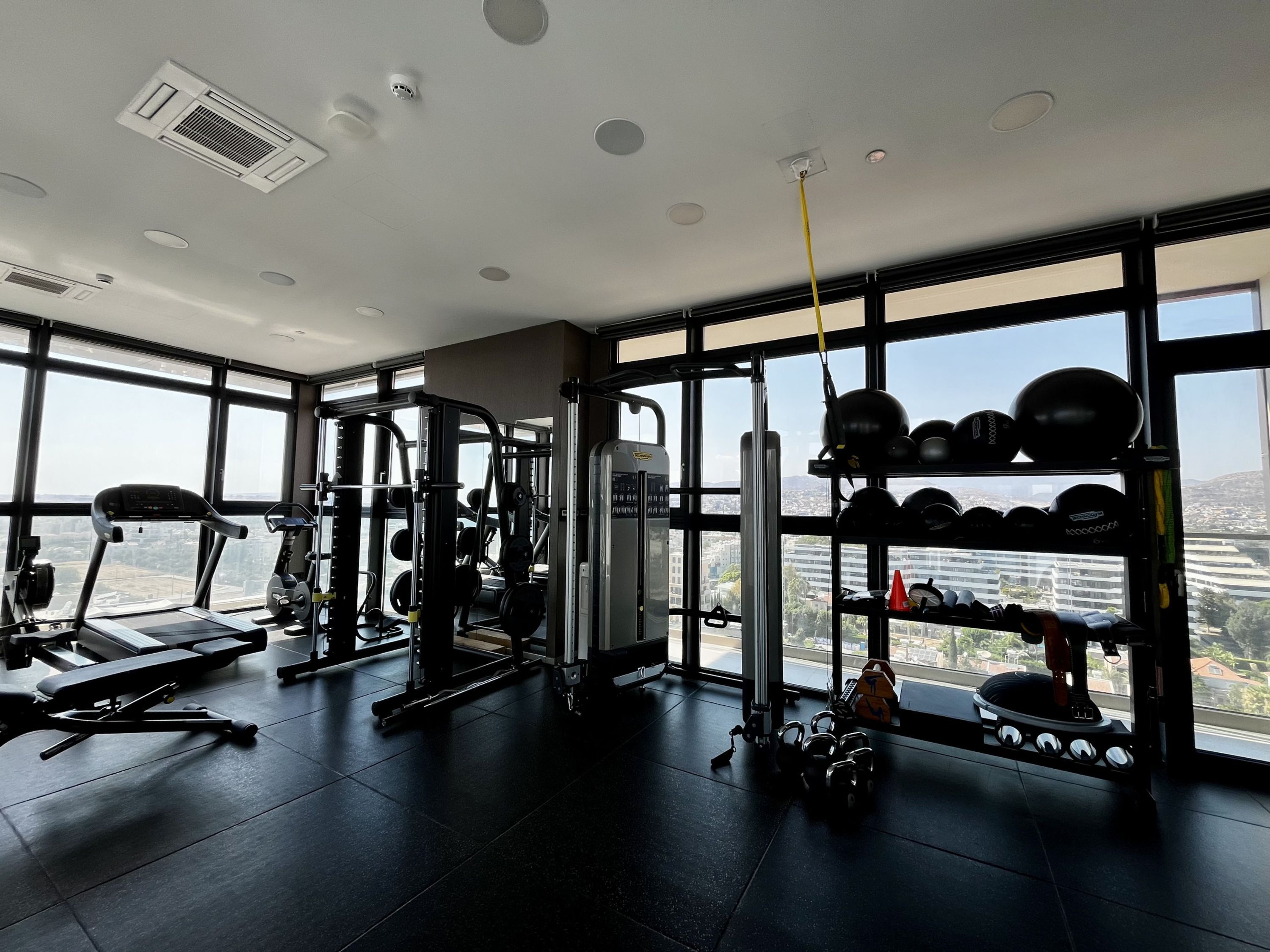 A gym with various exercise equipment, large windows, and a view of a cityscape.