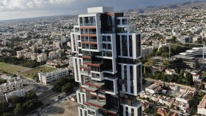 Un immeuble moderne de grande hauteur, doté de nombreux balcons, situé dans un quartier urbain densément peuplé, entouré de divers bâtiments et rues.