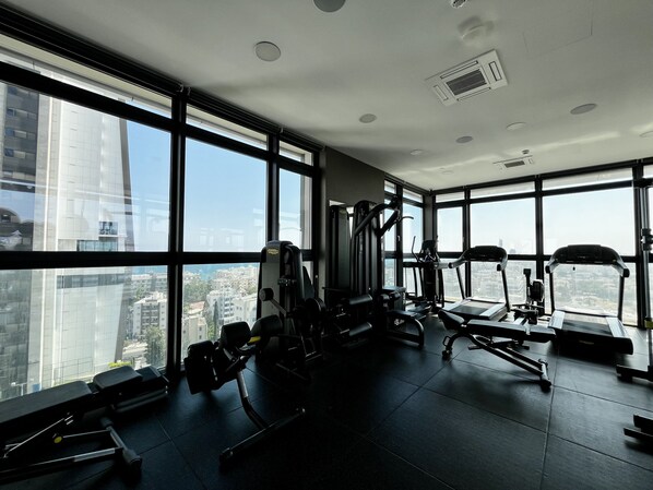 A gym with various exercise equipment, large windows, and a city view.