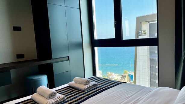 A hotel room with a bed, a large window, and a view of the city and sea. - 128 LIM - 2001 Stay Only Tower Suite (Limassol)
