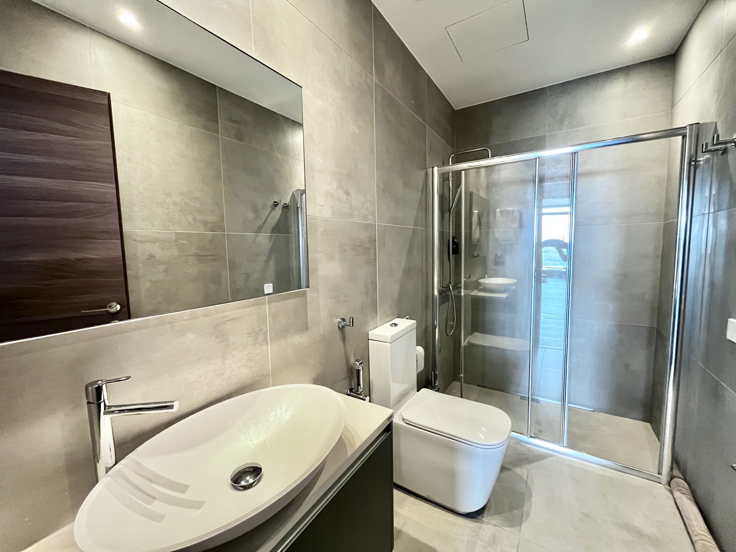 Een moderne badkamer met een grote spiegel, een witte wastafel, een toilet en een douchecabine met glazen wanden.
