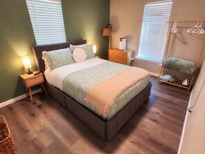 Un dormitorio con cama, mesitas de noche, lámpara, una silla colgante y un armario.