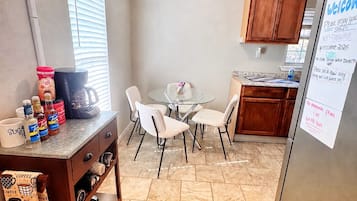 A compact kitchen with a dining area, a coffee station, and a refrigerator with a welcome message.