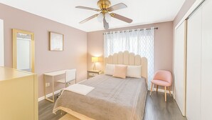 Quarto com cama, mesa de cabeceira, cadeira e ventoinha no teto.