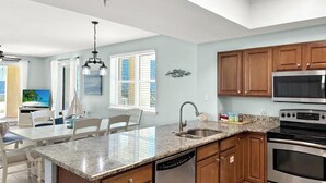 A modern kitchen with granite countertops, stainless steel appliances, and wooden cabinets. - 🦩Sunset Chaser at Ariel Dunes🦩 (Destin)
