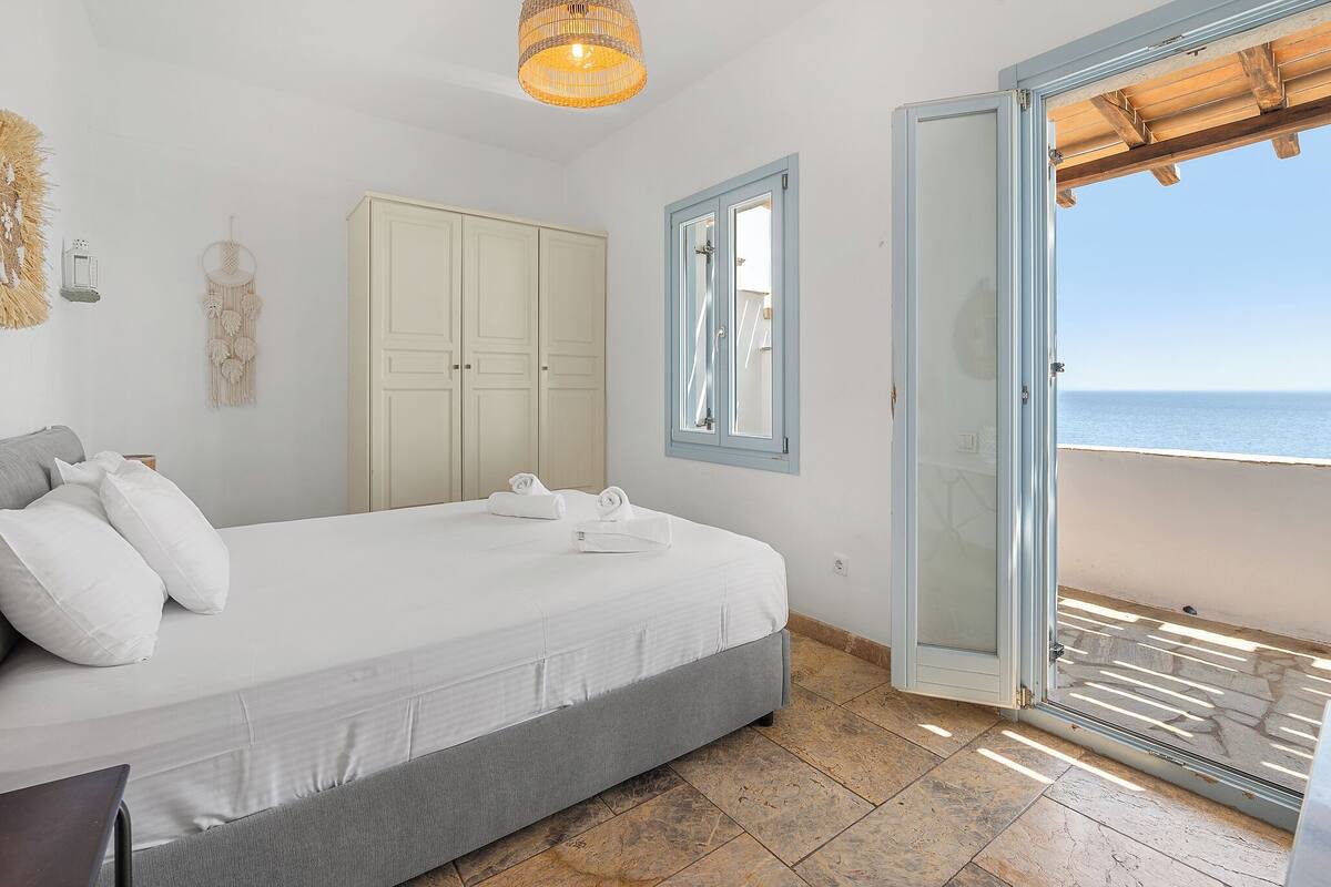 A bedroom with a bed, a wardrobe, a window, and a view of the sea.