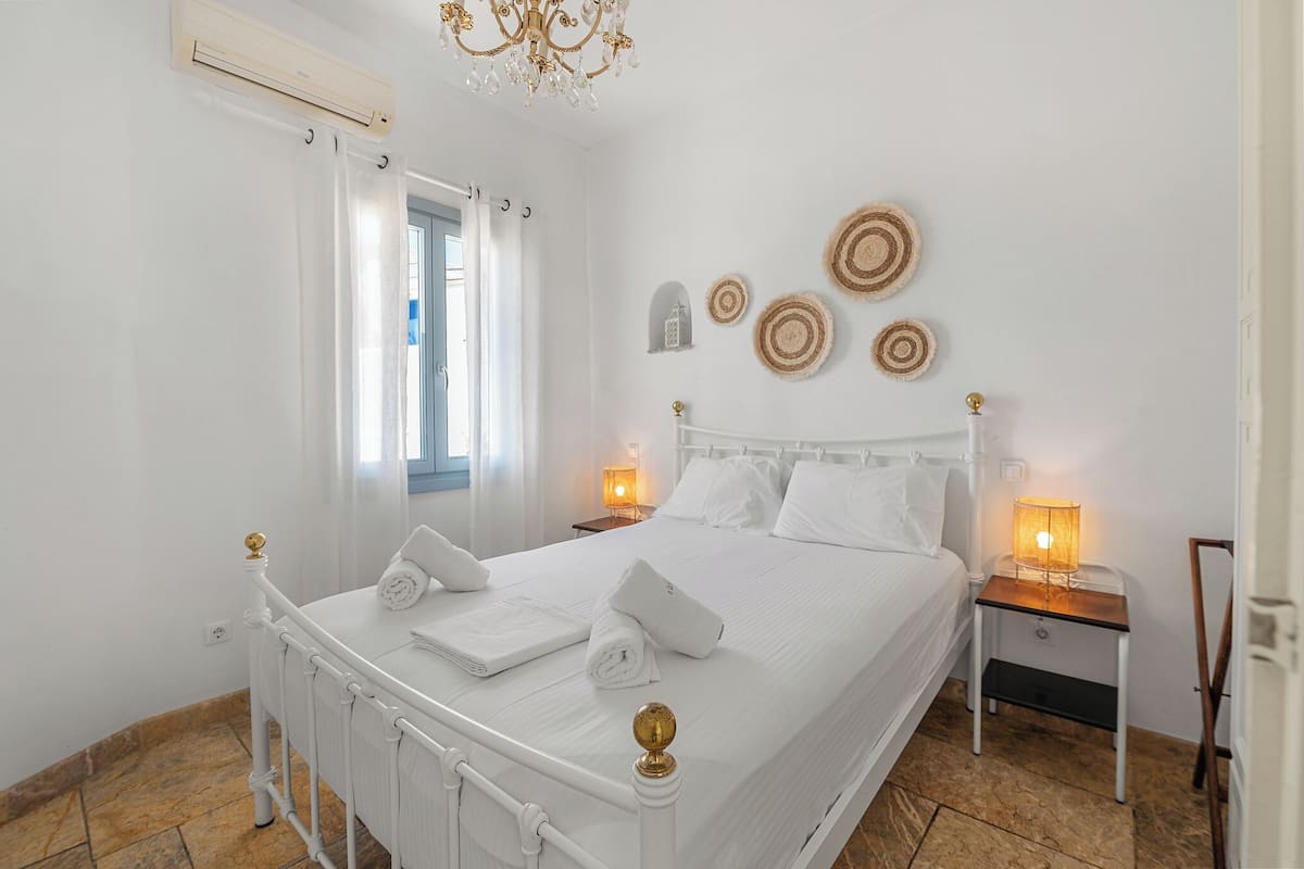 Ein weißes Himmelbett mit einer Chandelierleuchte, ein Nachttisch mit einer Lampe und eine Wand mit Wandteppichen.