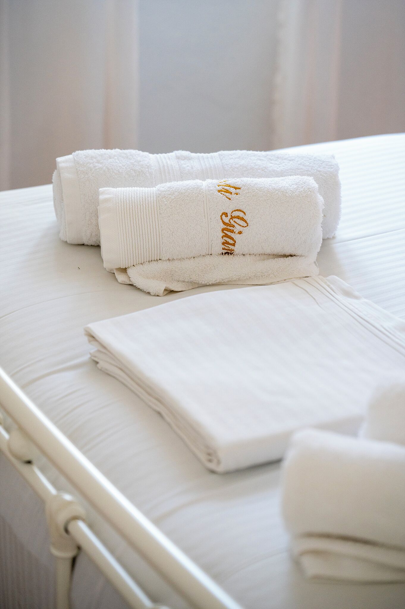 Strak opgemaakte witte handdoeken met goudkleurige letters op een bed.