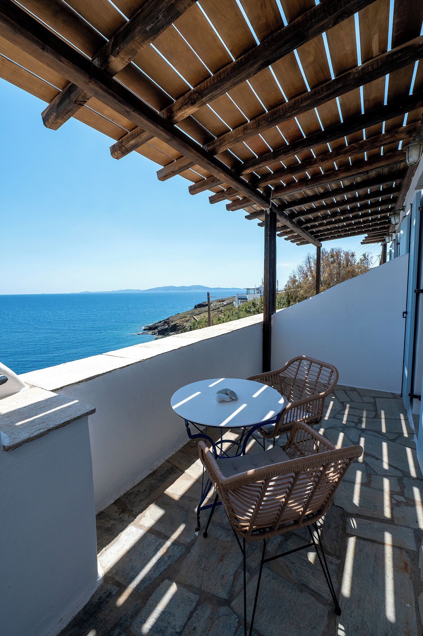 Un espace extérieur abrité, doté d’une table et de chaises, offrant une vue sur la mer et doté d’un sol en pierre.