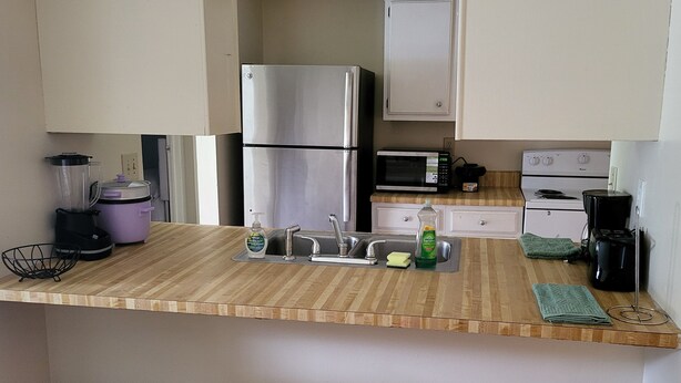 A kitchen with a wooden countertop, stainless steel appliances, a sink with soap and sponge, and a microwave above it.