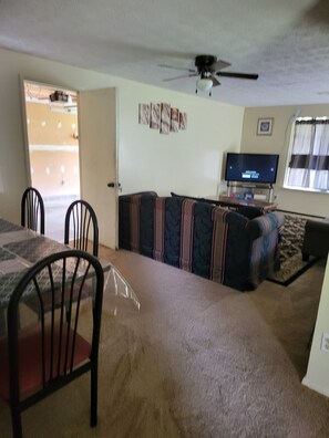 A living room with a sofa, a television, a ceiling fan, and a dining area with chairs and a table.