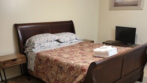 A bedroom with a large bed, a nightstand, a TV, and a painting on the wall.