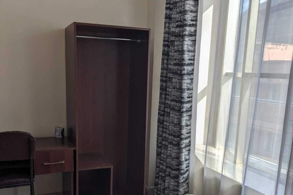 Habitación de hotel con cama, escritorio, armario y ventana con cortinas translúcidas.