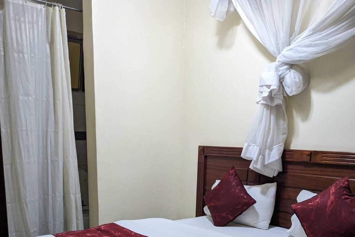 Una cama bien hecha con una colcha blanca y roja, dos almohadas y una toalla blanca al lado.