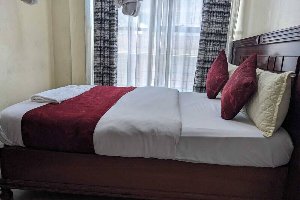 Una cama con una colcha blanca y roja, dos almohadas rojas y una blanca.