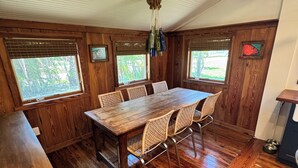 Comedor de madera con una mesa grande y sillas, paredes de madera y ventanas con persianas.