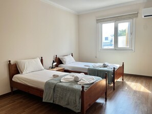 Una habitación de hotel con dos camas de madera, una mesita de noche, un ventanal y piso de madera.