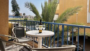 A balcony with wicker chairs, a round table, a bottle of wine, and glasses. - 115 AN - Stay Napa Oniro Apartment (Ayia Napa)