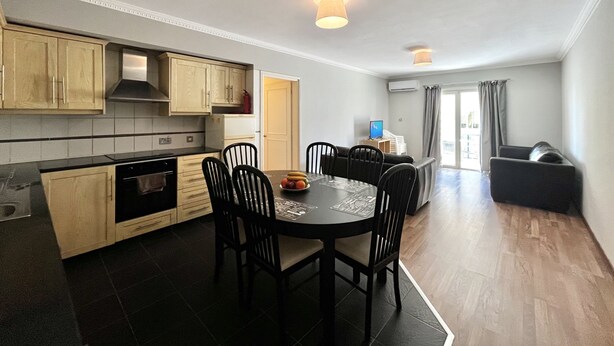 A modern kitchen with wooden cabinets, a dining table with chairs, and a living area with a sofa. - 115 AN - Stay Napa Oniro Apartment (Ayia Napa)