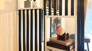 Een kamer met een zwart-wit gestreepte muur, een plank met boeken en een vaas bloemen, en een raam met uitzicht.